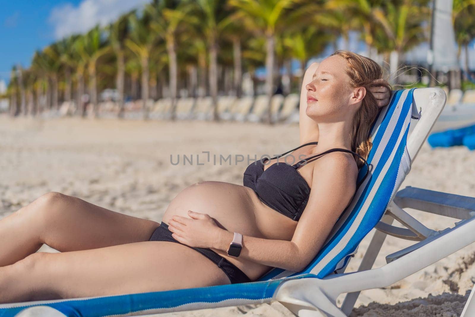 Basking in seaside tranquility, a pregnant woman lounges on a sun lounger, embracing the soothing ambiance of the beach for a moment of serene relaxation by galitskaya