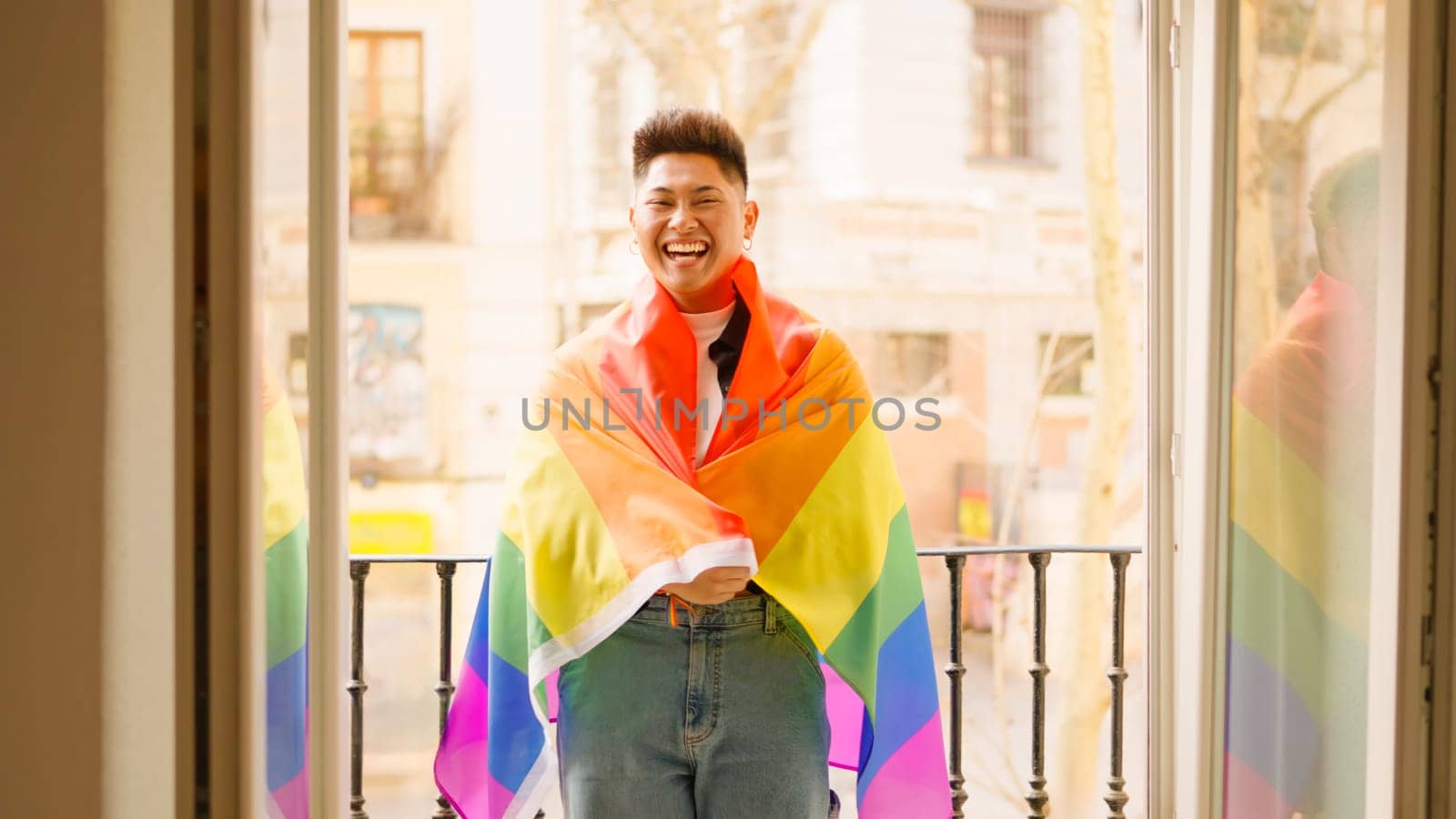 An hispanic man with a lgbt flag smiling at the balcony