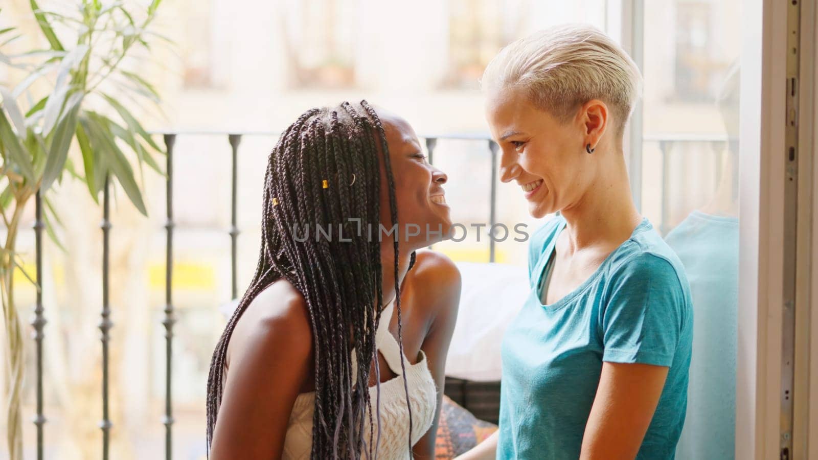 Relaxed lesbian couple taking and smiling sitting on a balcony at home