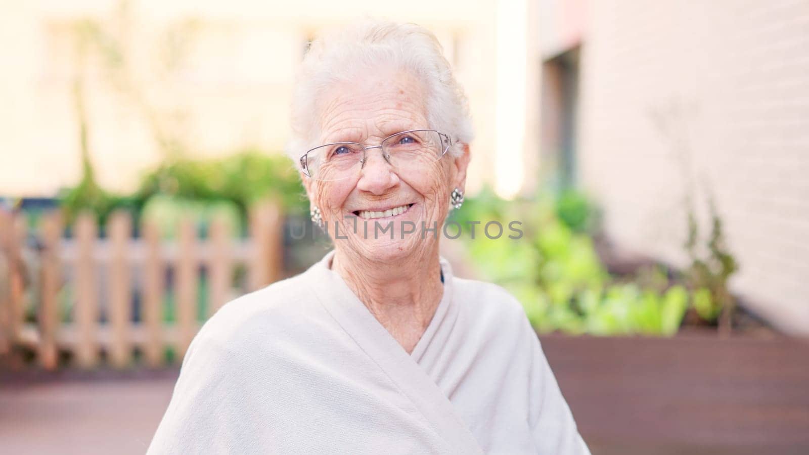 Photo of a tender old woman smiling at camera outside a nursing home