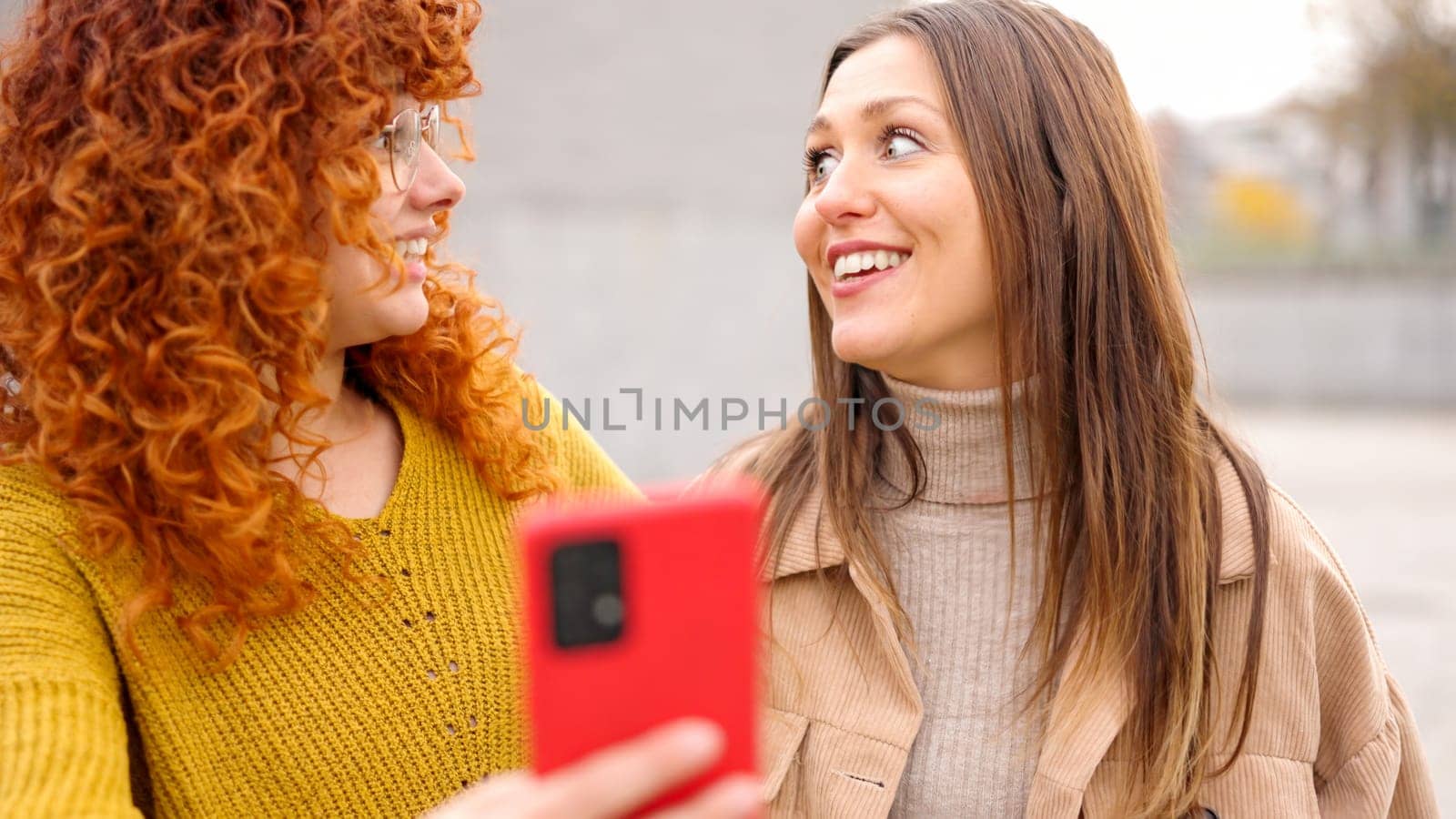 Two female friends surprised while using phone together in the street