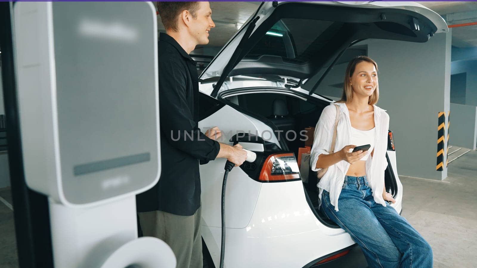 Electric car driver checks battery charging status app screen in car innards by biancoblue