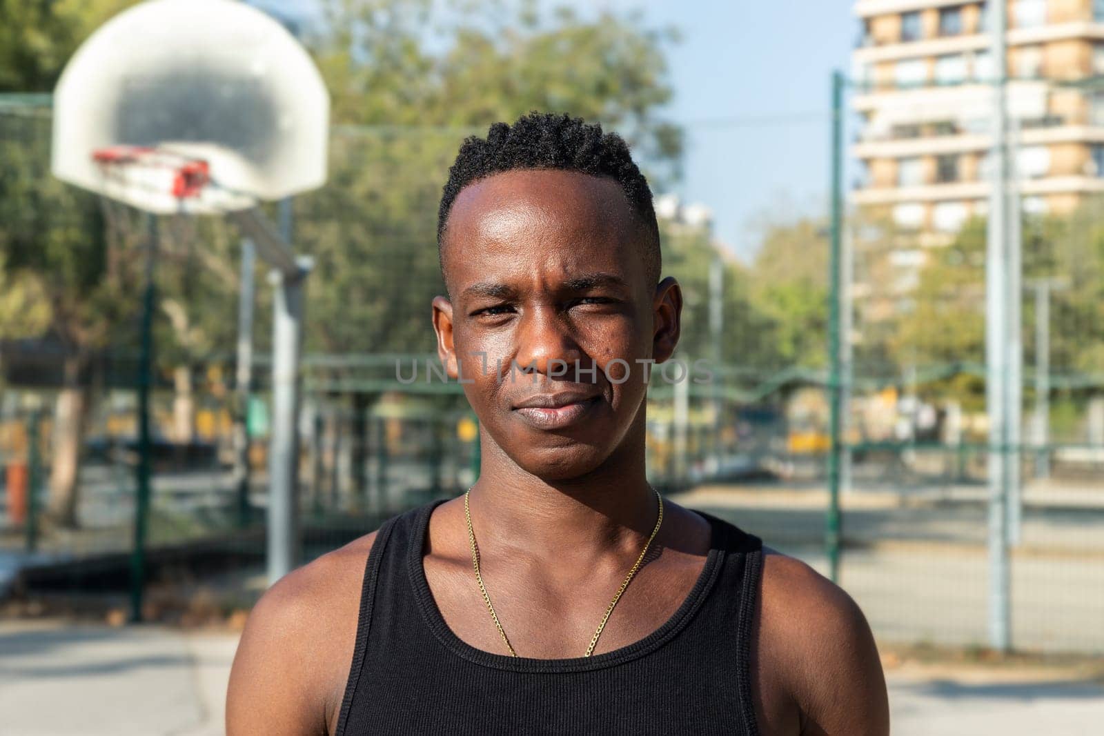Headshot portrait of black young man in basketball court outdoors looking at camera. Healthy lifestyle and sports concept.