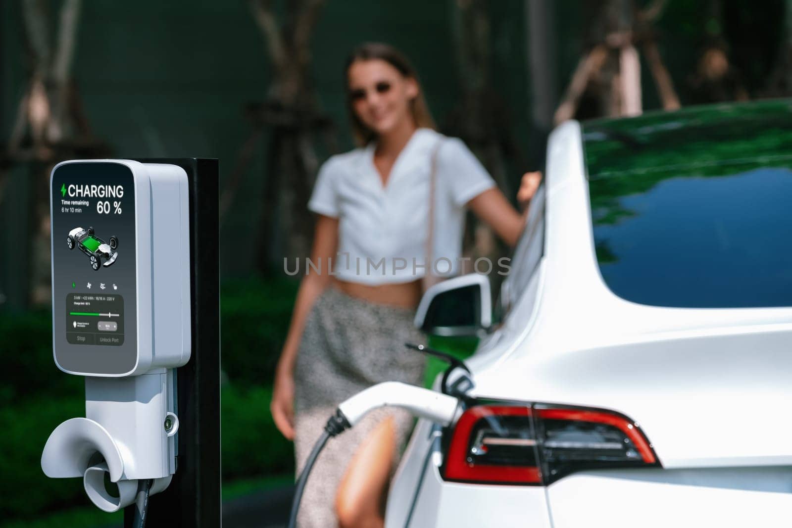 Young woman travel with EV electric car charging in green sustainable city outdoor garden in summer. Urban sustainability lifestyle by green clean rechargeable energy of electric BEV vehicle innards