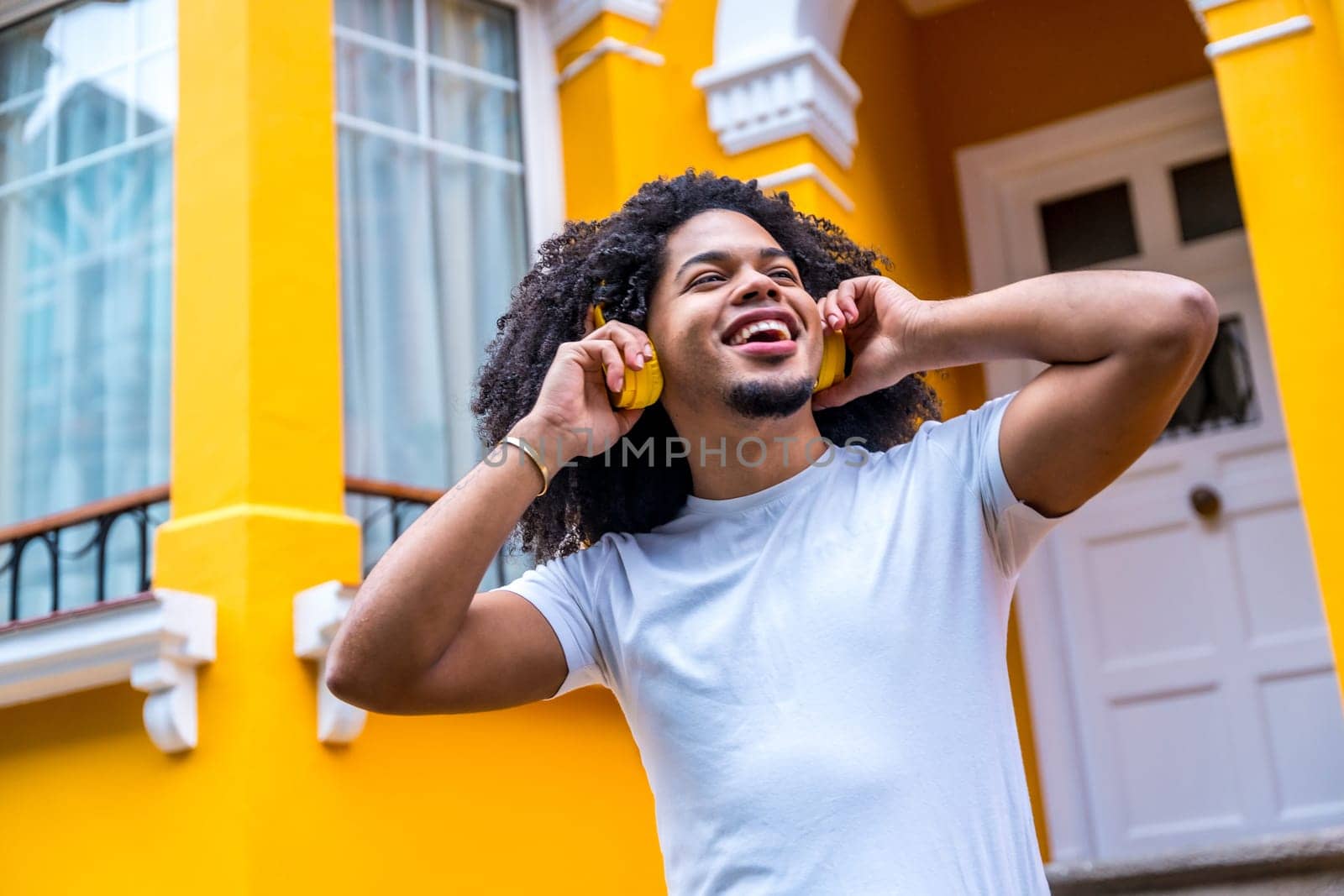 Happy african young man listening to music with headphones in a yellow colorful street