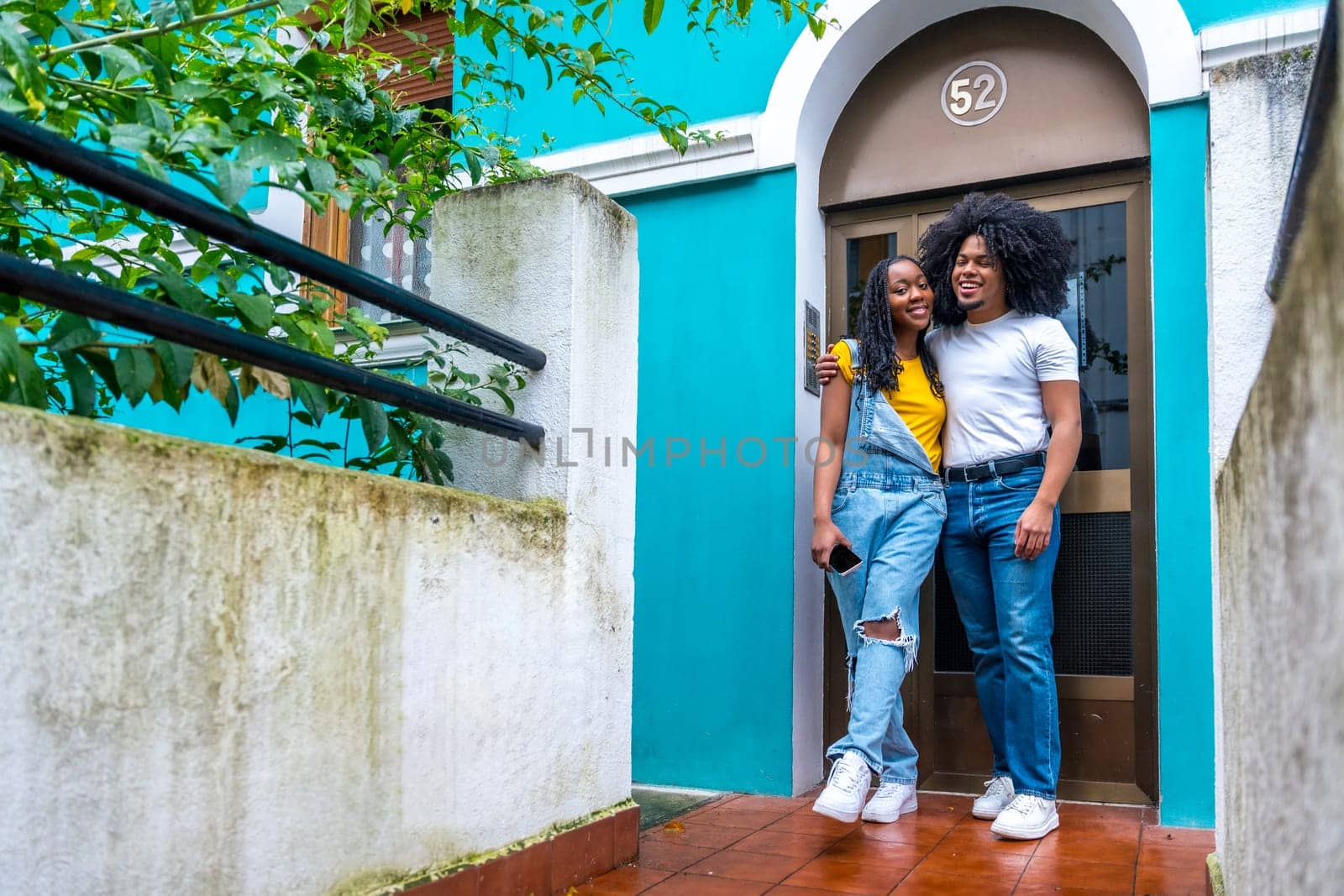 African young couple embracing proud in the door of their house with the facade painted in vivid blue