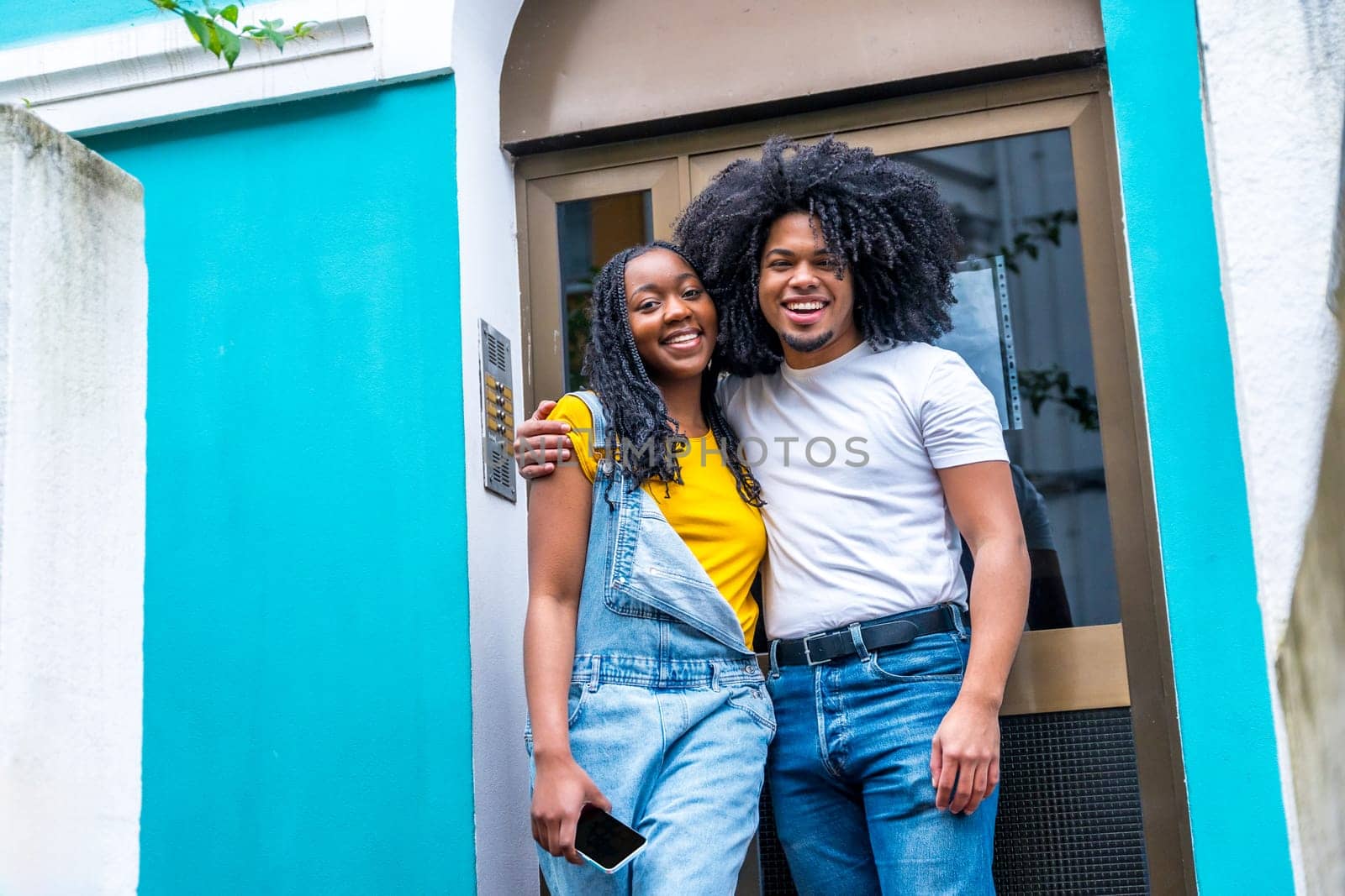 African young couple embracing happy in the entrance of their new house with the facade painted in vivid blue