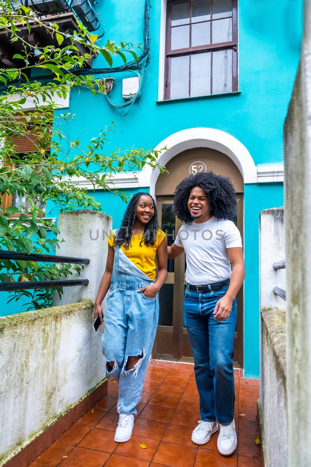 Vertical photo with copy space of a young casual african couple leaving a blue colorful house