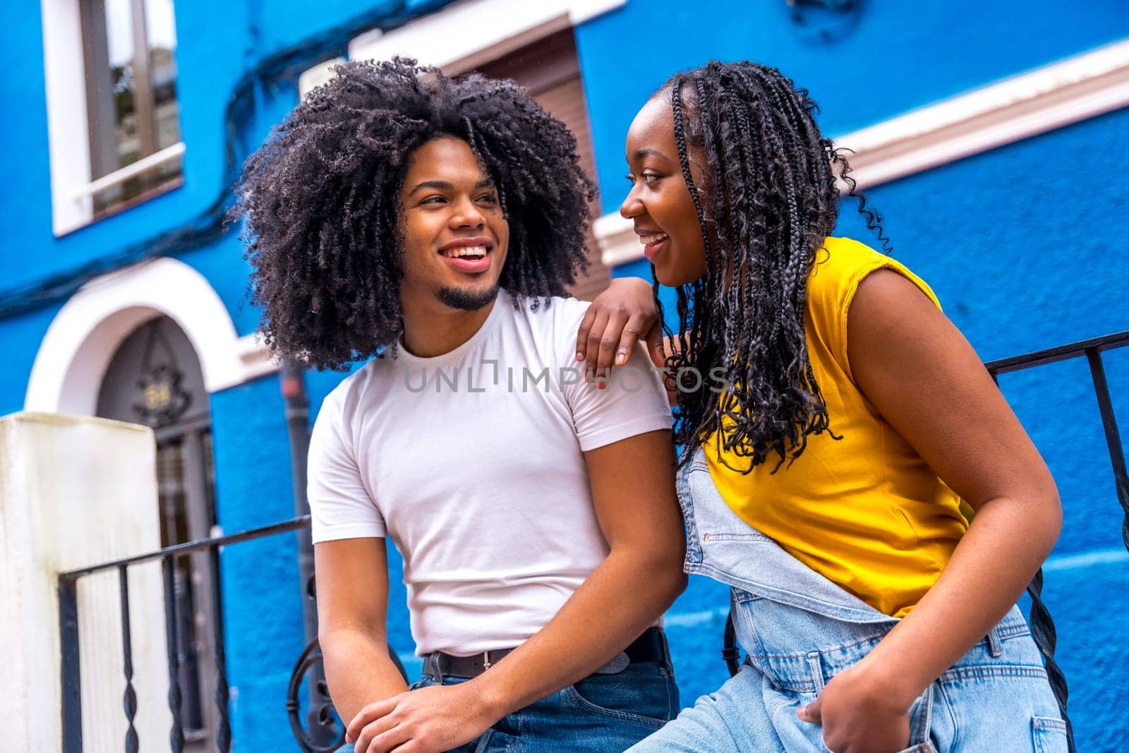 Cool african couple looking at each other sitting in the street with colorful houses