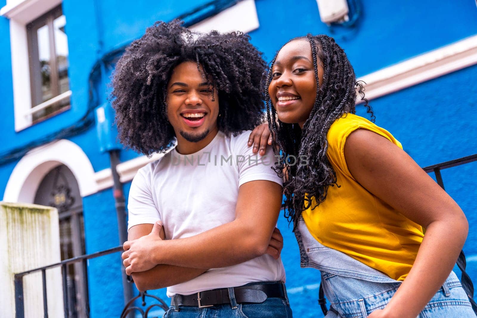 Happy african stylish couple smiling at camera leaning on a rail in a colorful street
