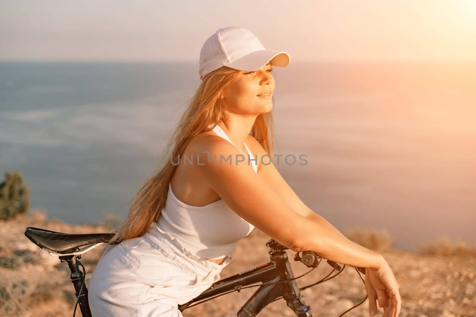 Woman travel bike sea. Happy woman cyclist sitting on her bike, enjoying the beautiful mountain and sea landscape, signifying the idea of an adventurous bike ride