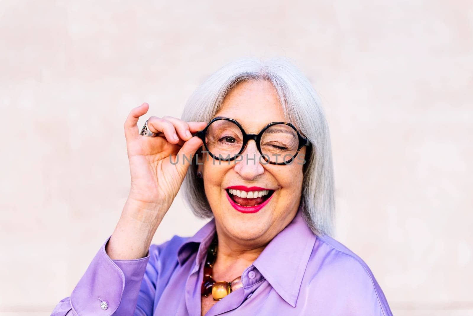 portrait of nice senior woman in glasses smiling and winking looking at camera, concept of elderly people happiness and active lifestyle, copy space for text