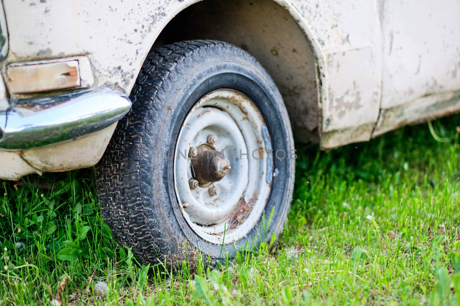 An old wheel on an old car. The concept of replacing a car with a new one to improve the quality of life