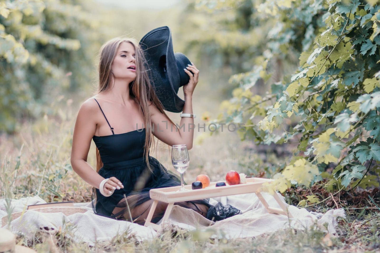 Woman picnic vineyard. Happy woman with a glass of wine at a picnic in the vineyard, wine tasting at sunset and open nature in the summer. Romantic dinner, fruit and wine. by panophotograph