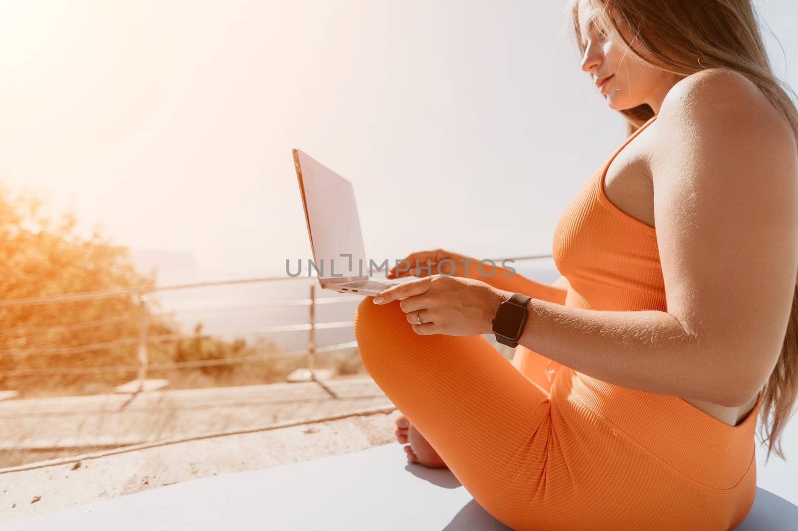 Woman laptop sea. Working remotely on seashore. Happy successful woman female freelancer working on laptop by the sea at sunset, makes a business transaction online. Freelance, remote work on vacation by panophotograph