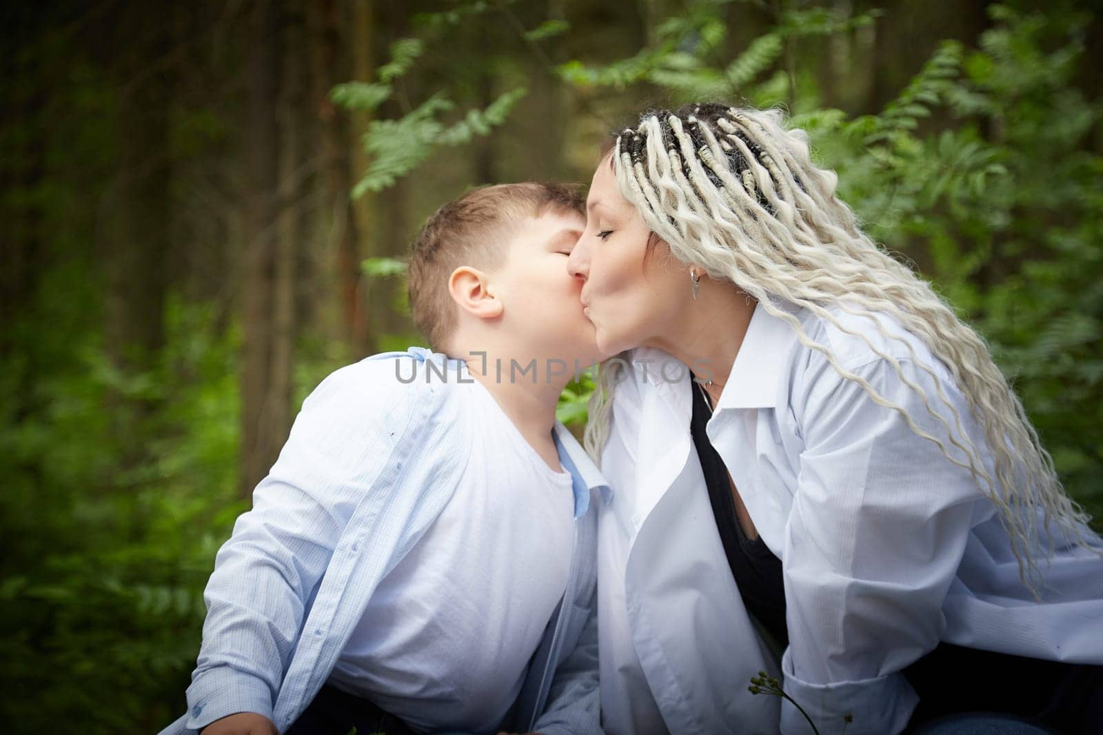 Funny mother with dreadlocks and fat boy happy kissing in the woods on a sunny summer day by keleny
