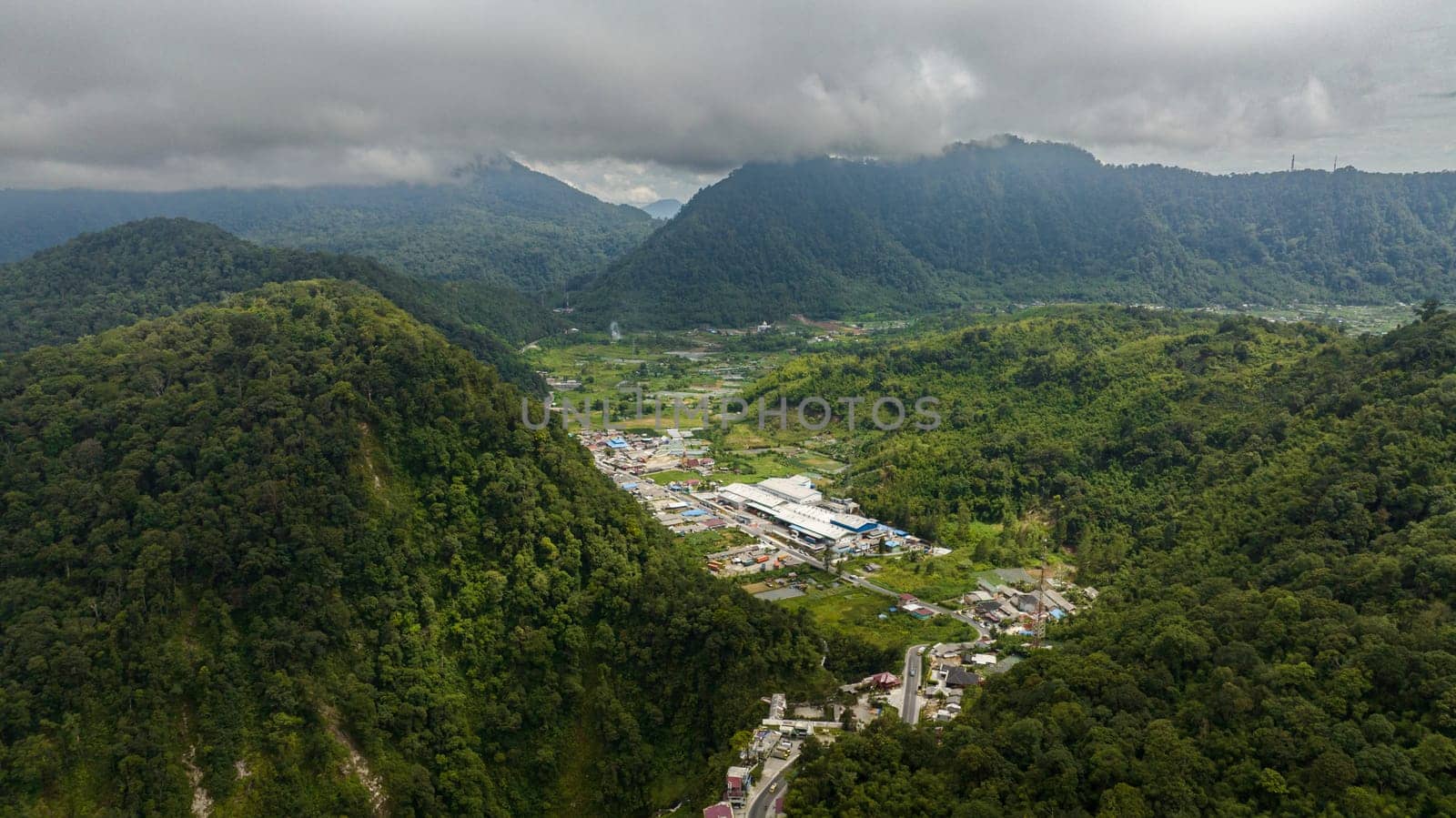 Aerial drone of small town among the mountains with jungle and rainforest. Berastagi, Sumatra. Indonesia.