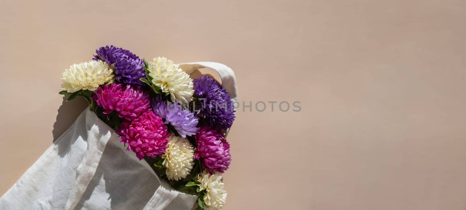 Bouquet of flowers in cotton natural bag for delivery. Copy space for text. Concept of holiday congratulation present or gift. Spring minimalistic