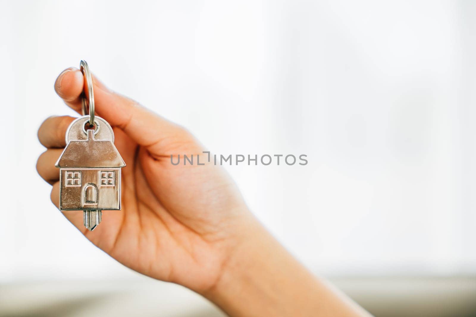 Woman's hand holds house key showcasing homeowners' achievement. Agent displays model home signifying real estate success. Confidence and happiness resonate.