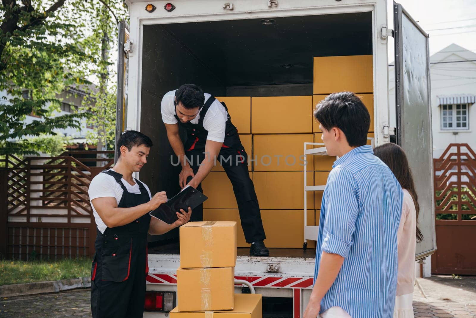 A couple signs delivery checklist after furniture upload delighted by professional movers' service. Employees display teamwork for customer satisfaction. Moving Day Concept by Sorapop