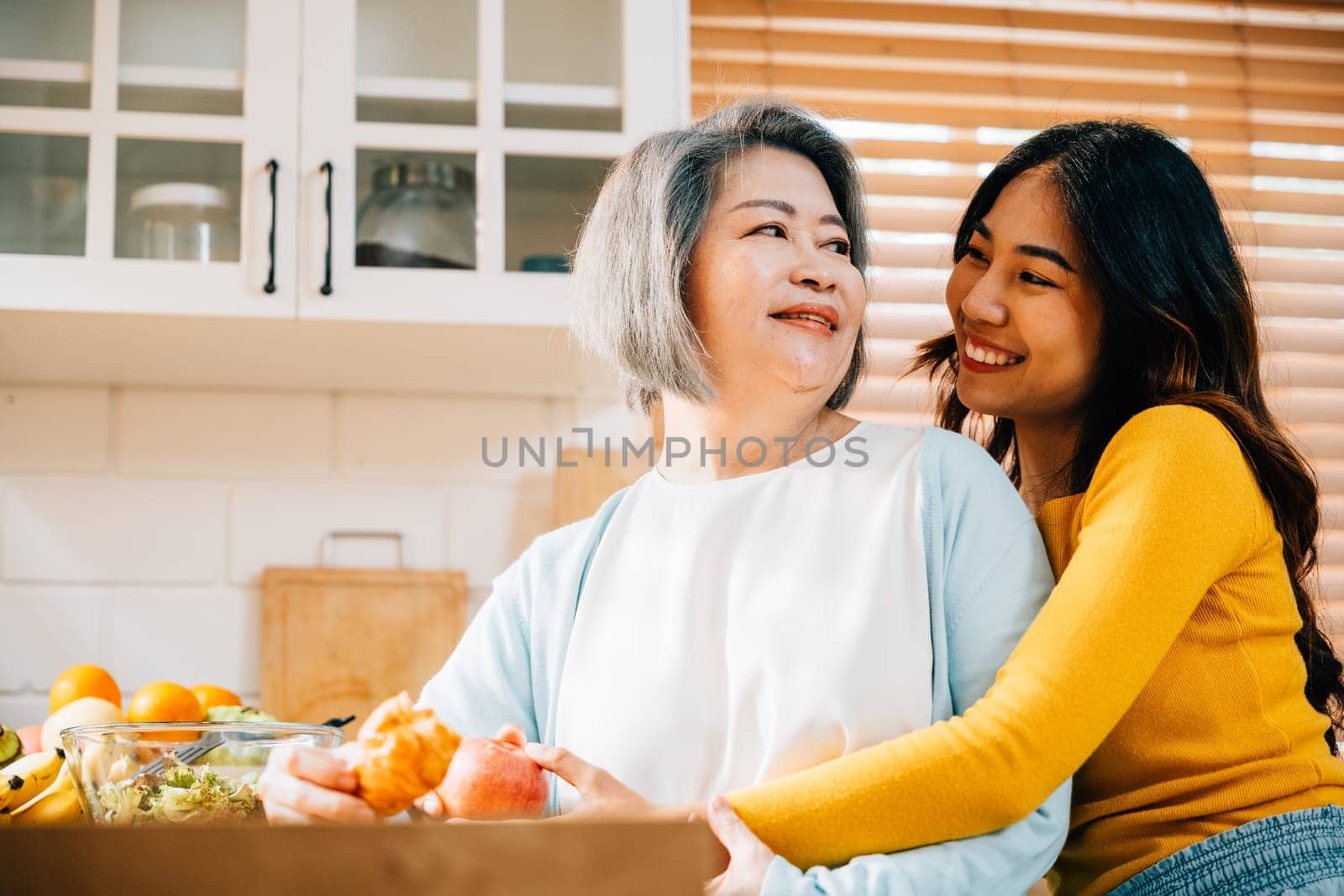 A portrait of an old mother and her adult daughter in the kitchen, holding an apple. Their smiles reflect the happiness and togetherness of family learning and teaching.