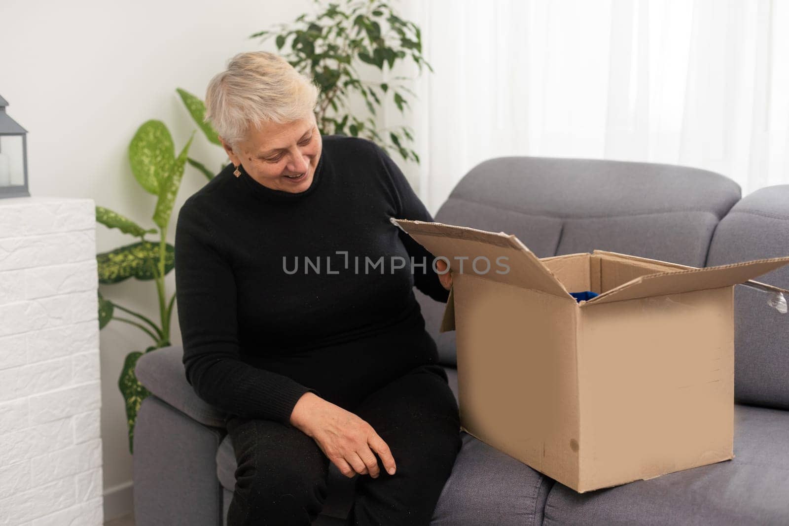 Elderly woman unpacking things in new house. opening cardboard box. Real estate, purchase concept by Andelov13