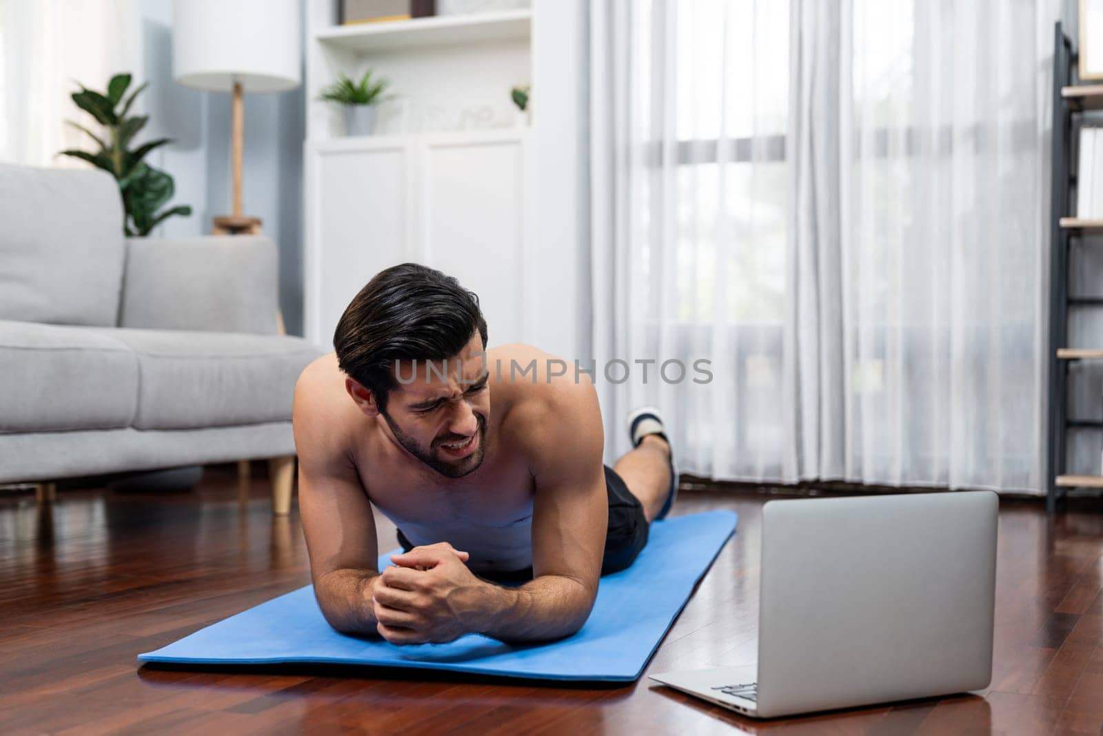 Athletic and sporty man suffer from exercise injury during online body workout exercise session at home. Painful ache from injured muscle accident during gaiety home exercise workout training concept.