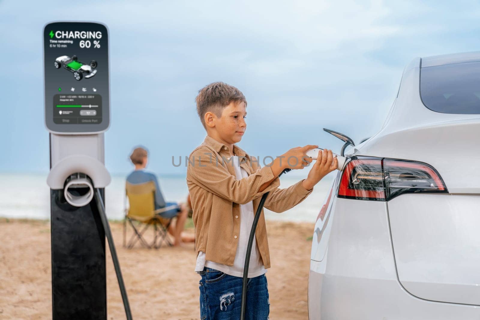 Family vacation trip traveling by the beach with electric car, little boy recharge EV car while his family enjoy seascape beach. Family trip with alternative energy and eco-friendly car. Perpetual