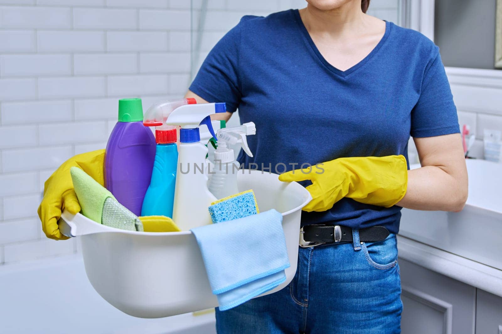 Woman in gloves with basin of detergents in bathroom. Female preparing for routine house cleaning, housecleaning service worker posing at workplace. Housekeeping, housework, cleaning concept