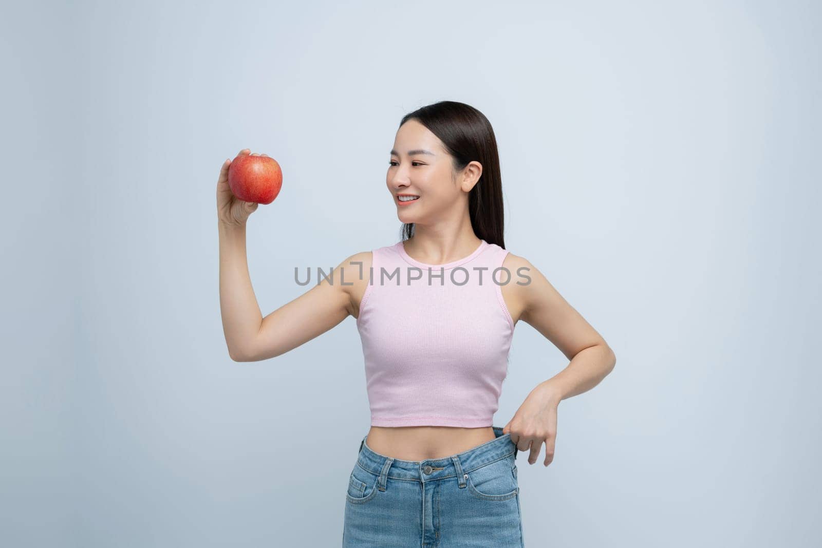 young woman show loose pants on waist after weightloss hold red apple isolated on white background by makidotvn