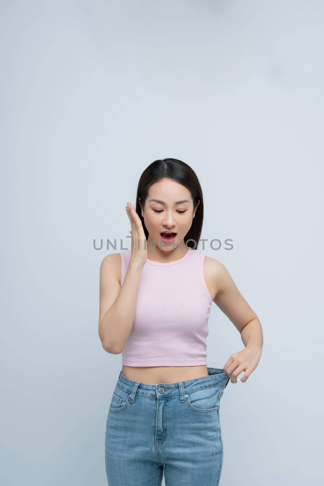 Young smiling happy woman show loose pants on waist after weightloss isolated on white background.  by makidotvn