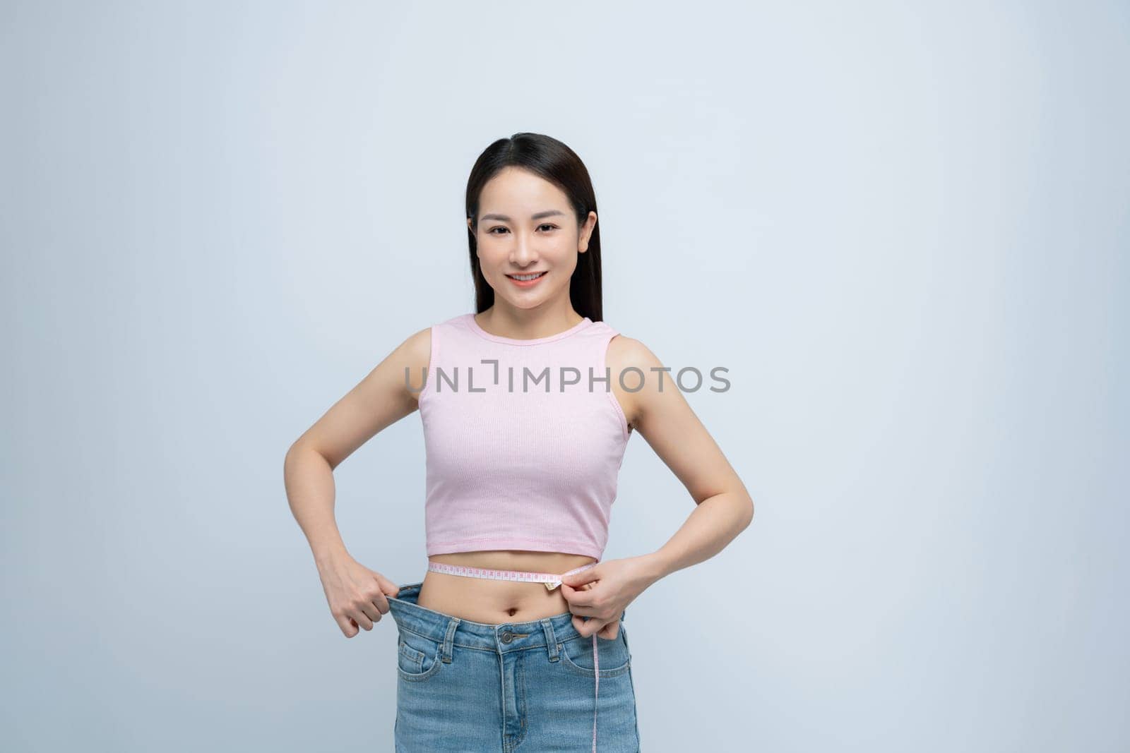 Young fun woman show loose pants after weightloss hold measure tape on waist by makidotvn