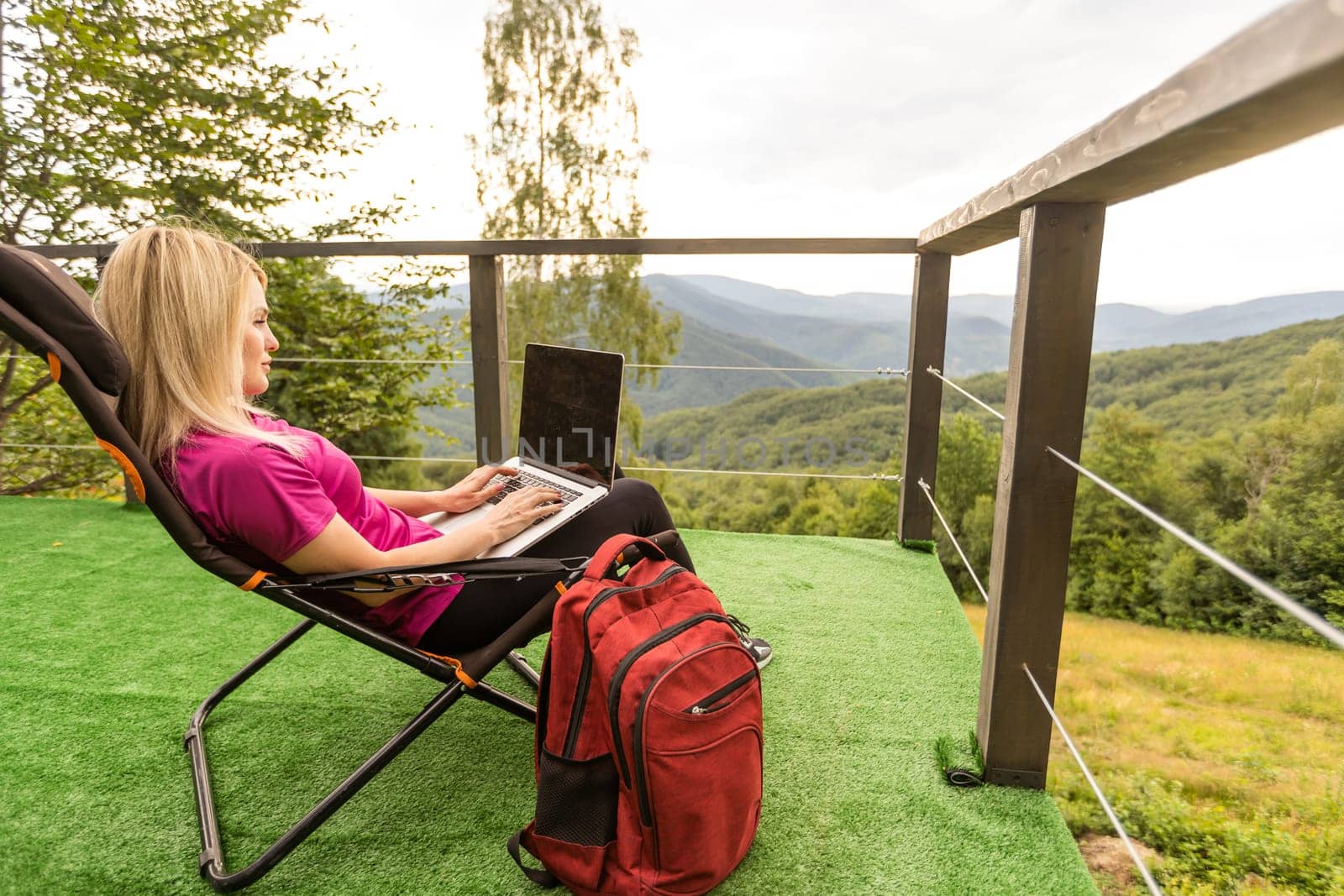 Young business woman working at the computer on the rock. Young girl downshifter working at a laptop at sunset or sunrise on the top of the mountain, working day