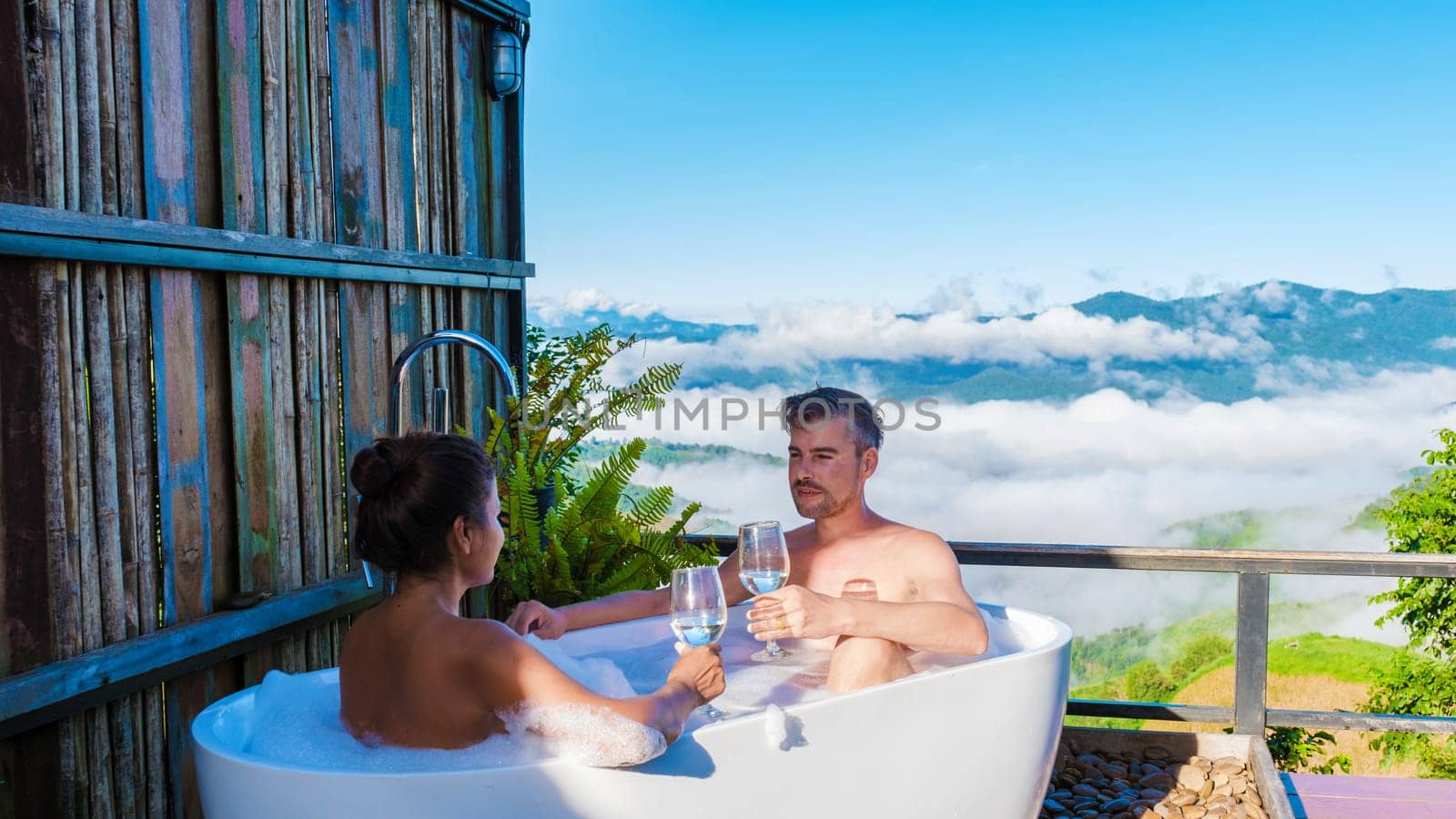 a couple of men and women in a bathtub looking out over the mountains of Chiang Rai Northern Thailand during vacation. Outdoor bathroom, young couple in a bath tub