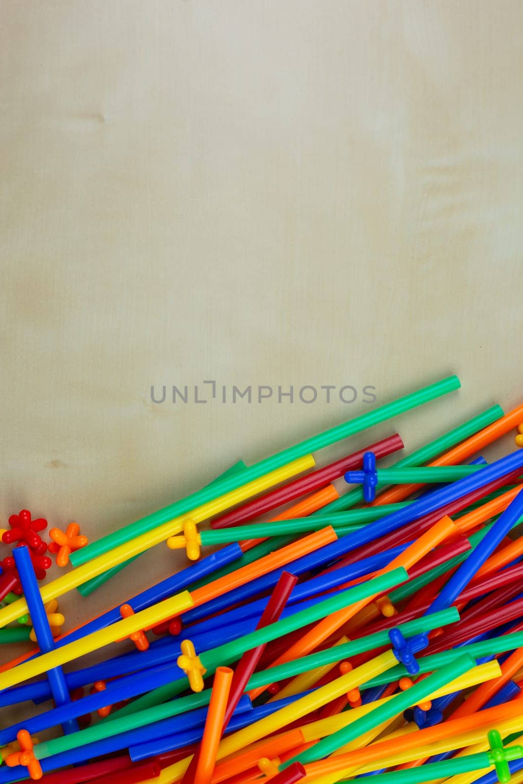 Colored parts of modern construction set are scattered on a wooden table with space for text, plastic tubes of flexible construction set