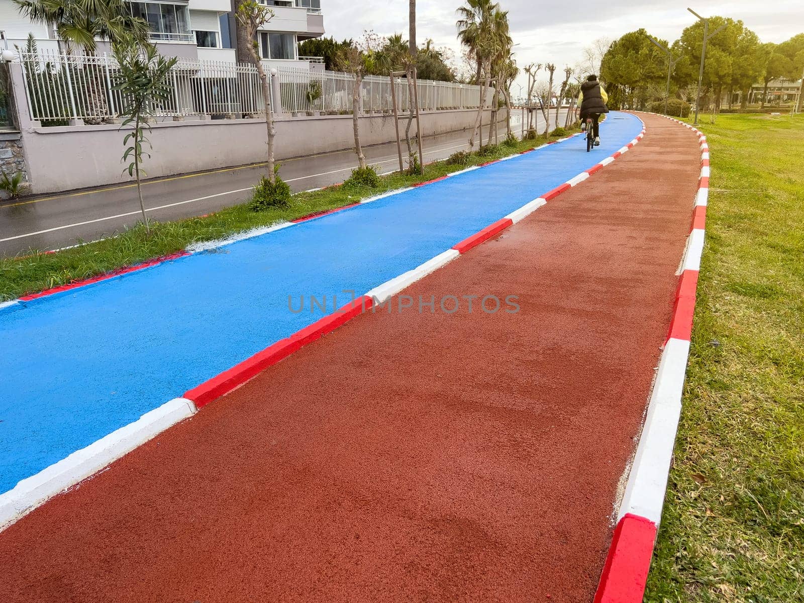 Blue bike path and red running path run side by side through a public park by Sonat