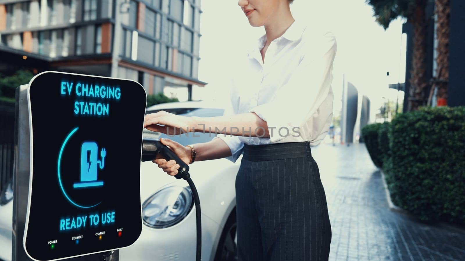 Businesswoman recharge her electric car from charging station at city center or public parking car. Eco friendly rechargeable car using alternative clean energy. Peruse