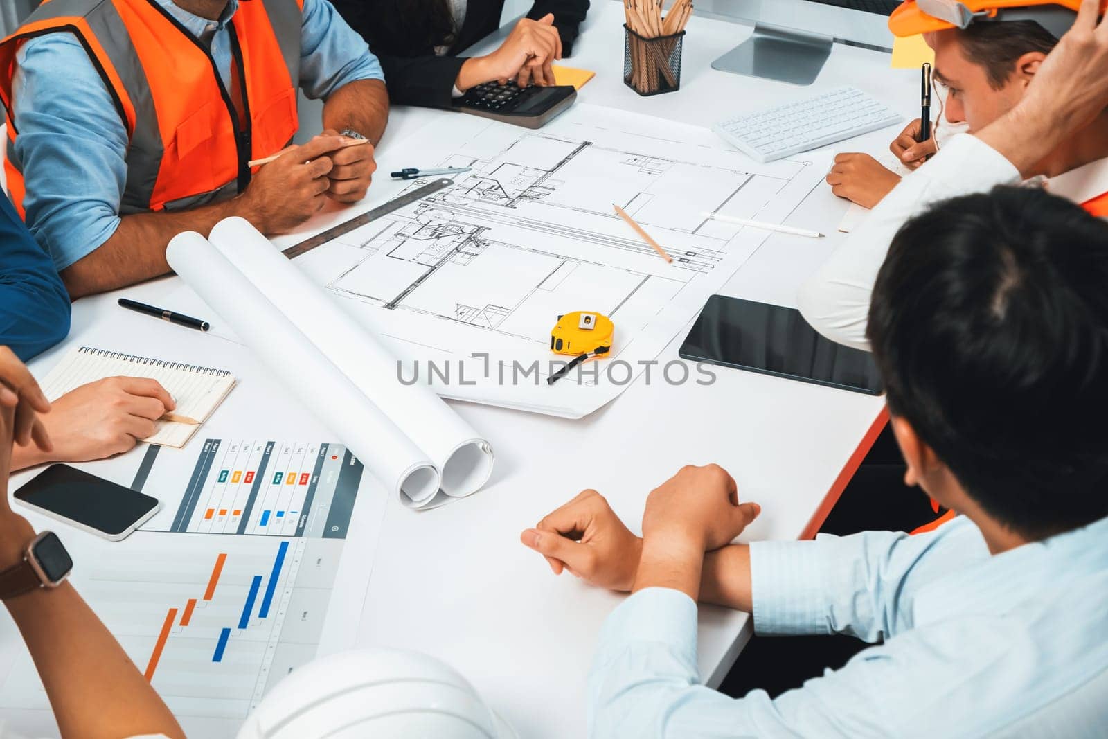 Diverse group of civil engineer and client working together on architectural project, reviewing construction plan and building blueprint at meeting table. Prudent