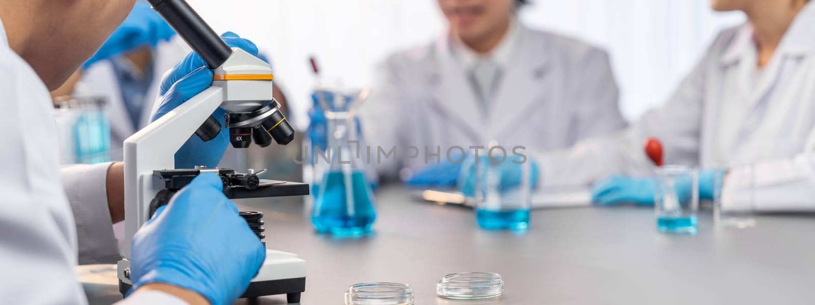 Group of dedicated scientist conduct chemical experiment using microscope in medical laboratory to develop new vaccine drug or antibiotic. Biotechnology lab and medicine research concept. Neoteric