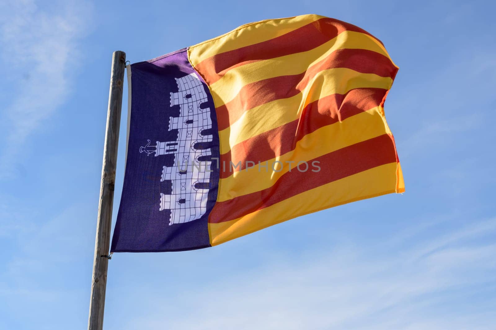 A vibrant flag with red and yellow stripes along a blue background with an emblem, against a blue sky, Majorca, Balearic Islands, Spain