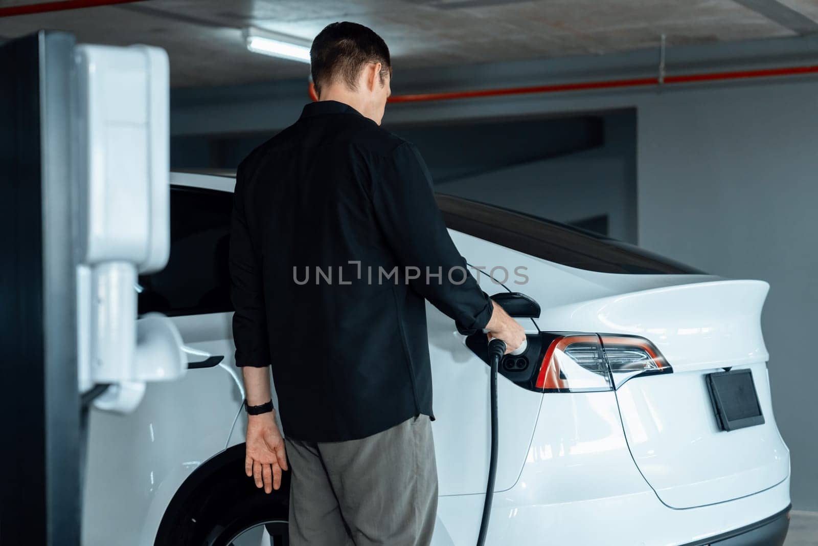 Young man travel with EV electric car to shopping center parking lot innards by biancoblue