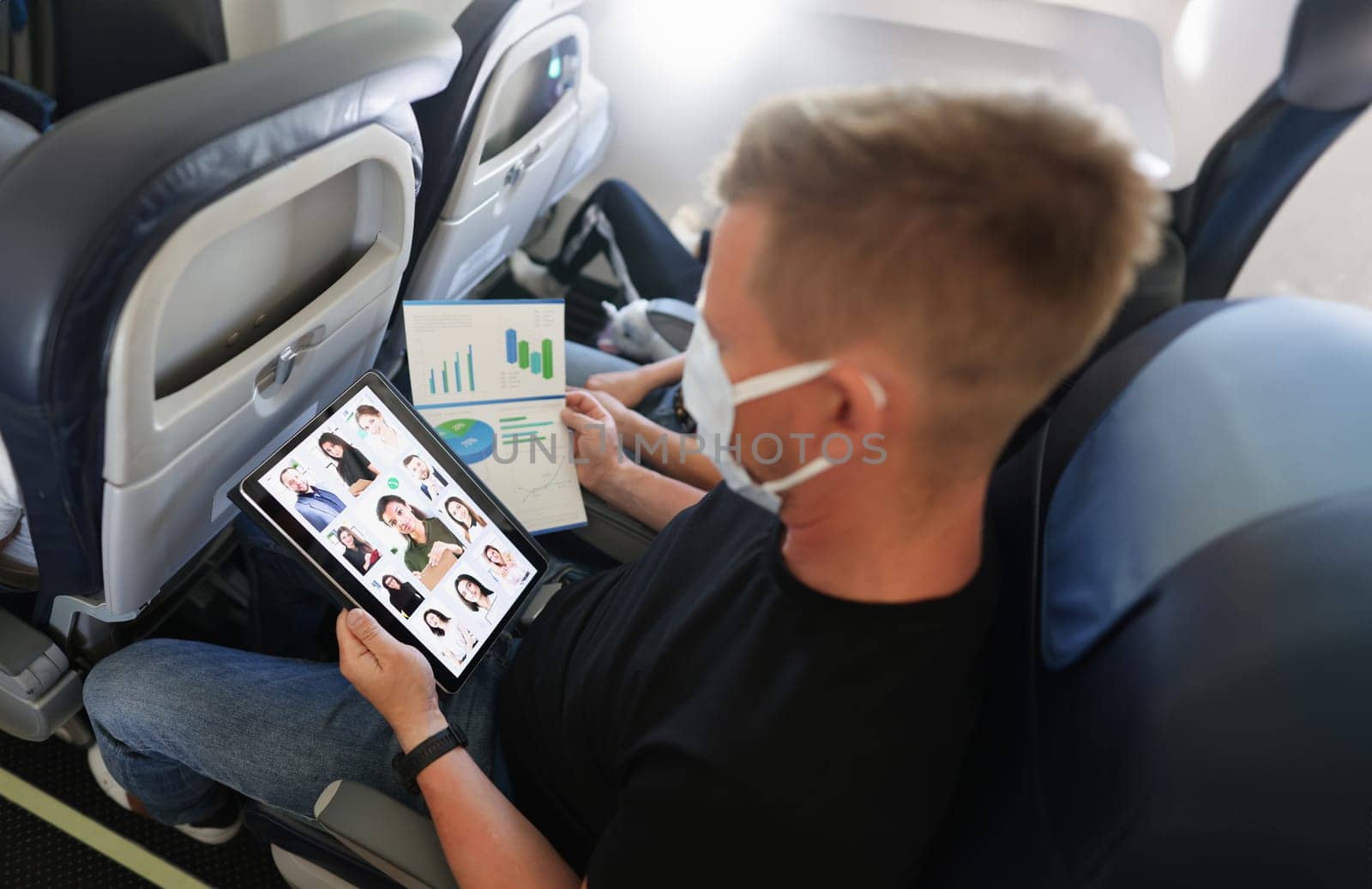 A man in a protective mask with a tablet and documents on the plane, close-up. Teamwork, report chart