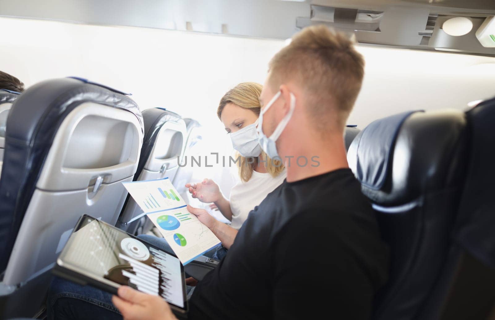 A man and a woman in protective masks with documents on the plane, close-up. Flight meeting, business trip