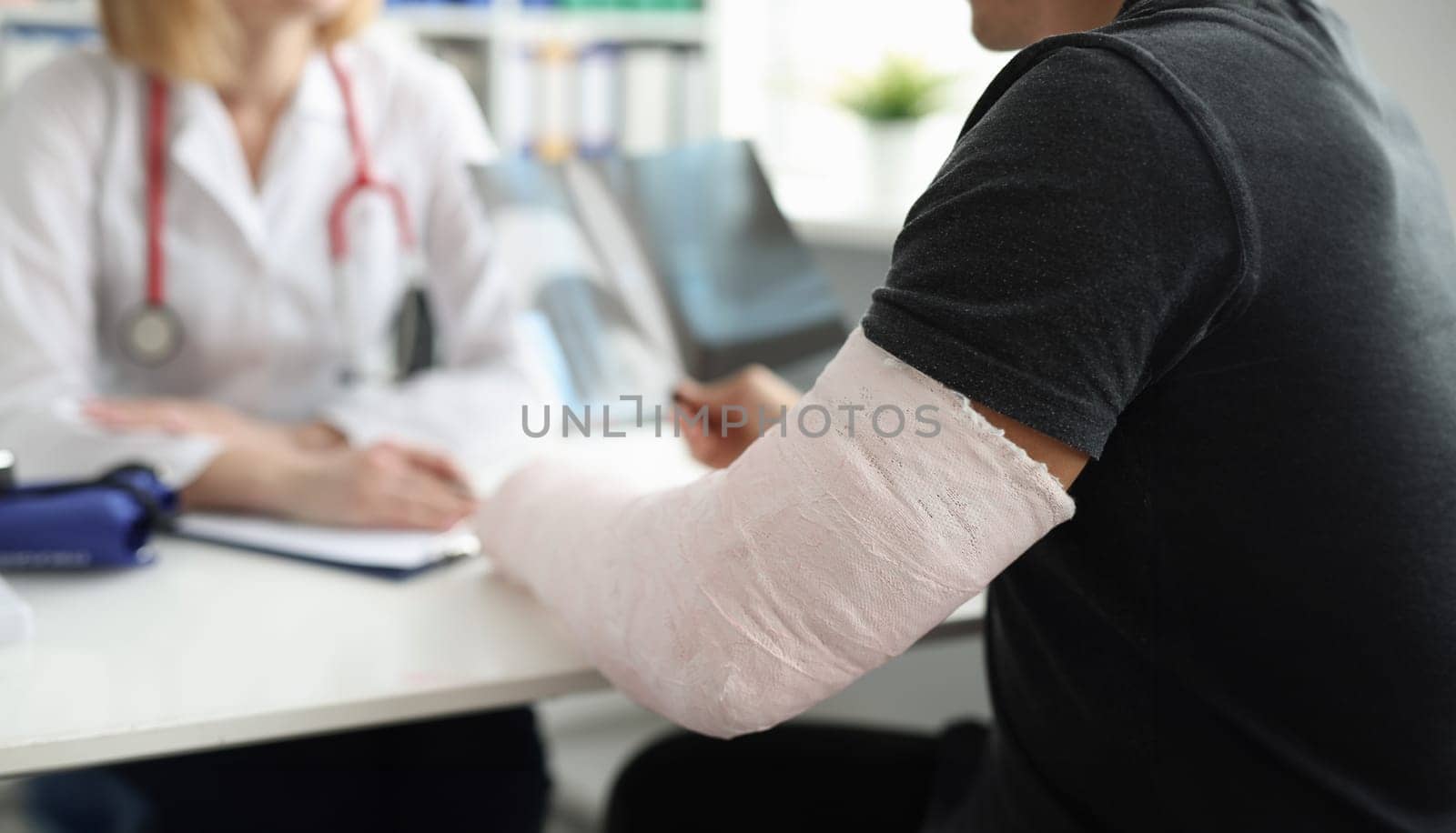 A man with a broken arm sits in front of a doctor, close-up, blurry. Traumatology consultation, trauma treatment
