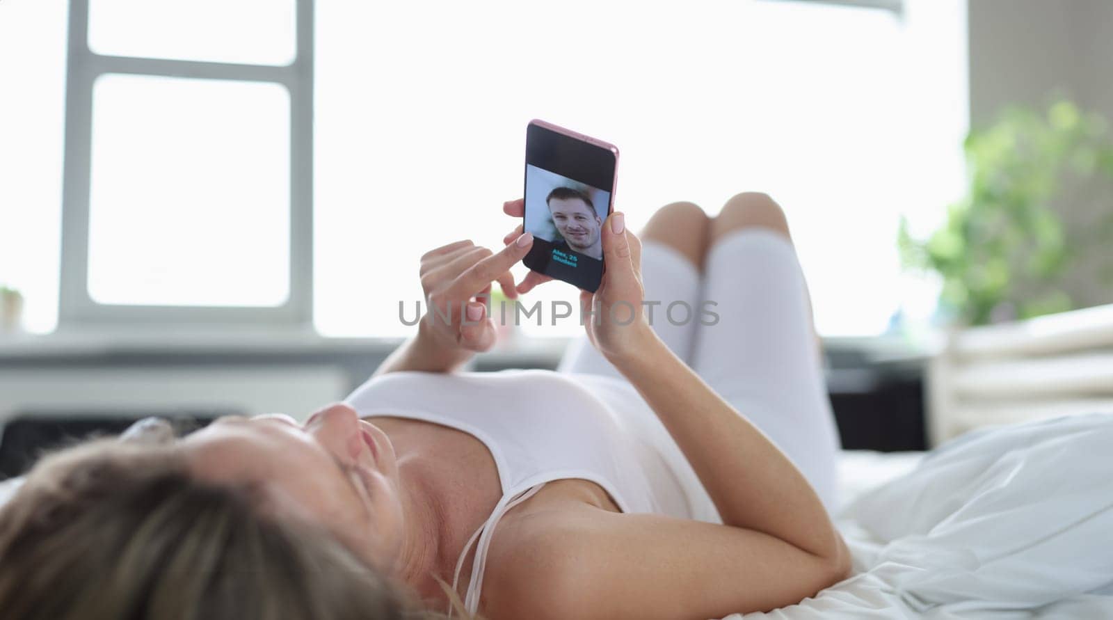 A woman lies on her back on the bed and looks into the phone, close-up. Dating site, search for a marriage partner online