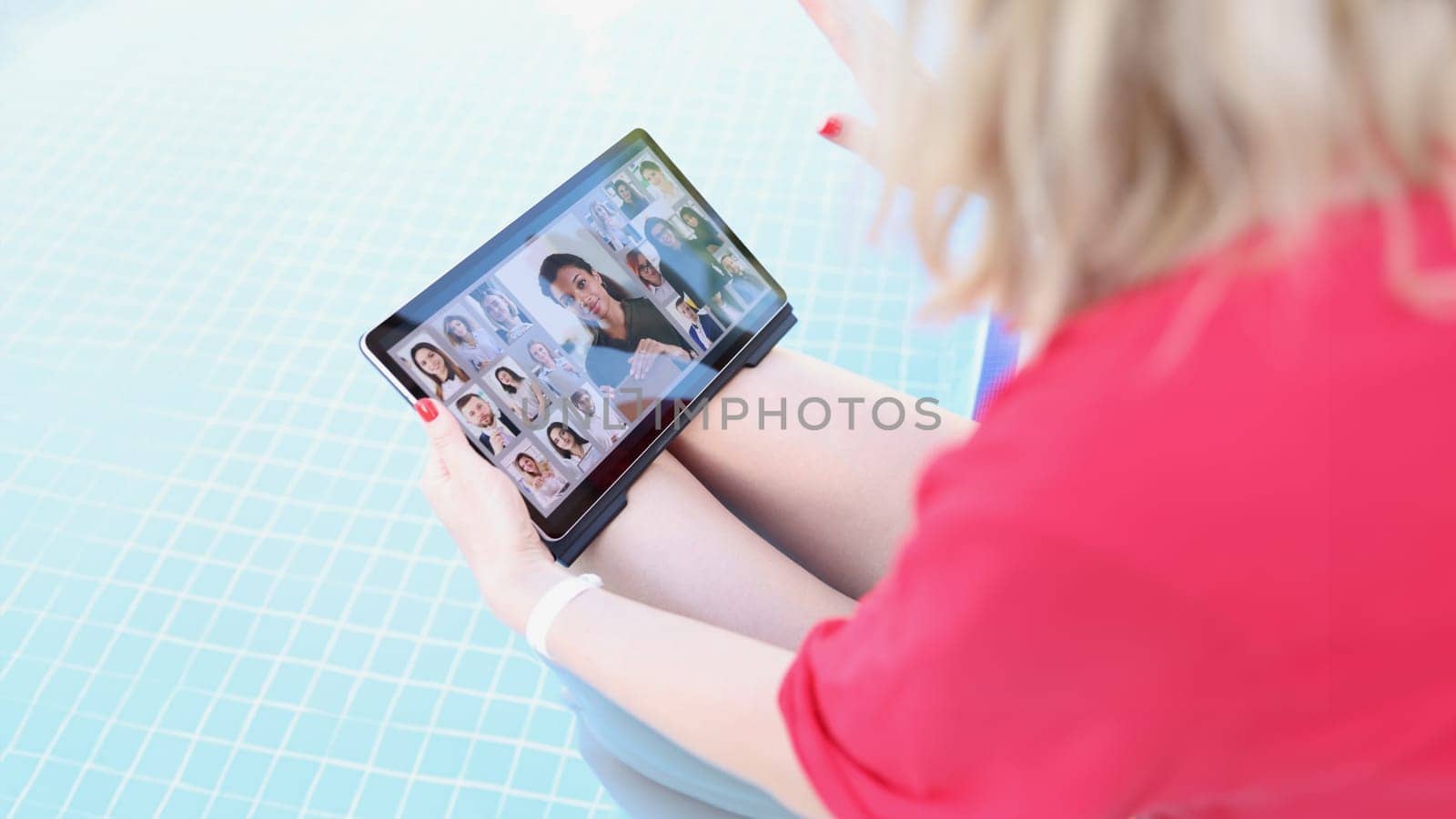 A woman by the pool holds a tablet on her lap, blurry by kuprevich