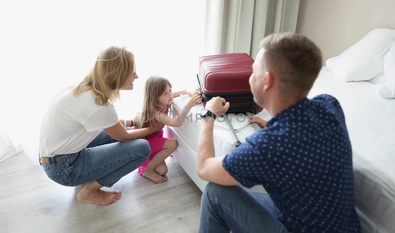 A couple with a little girl in a hotel close their suitcase. Summer family vacation, check out from the room