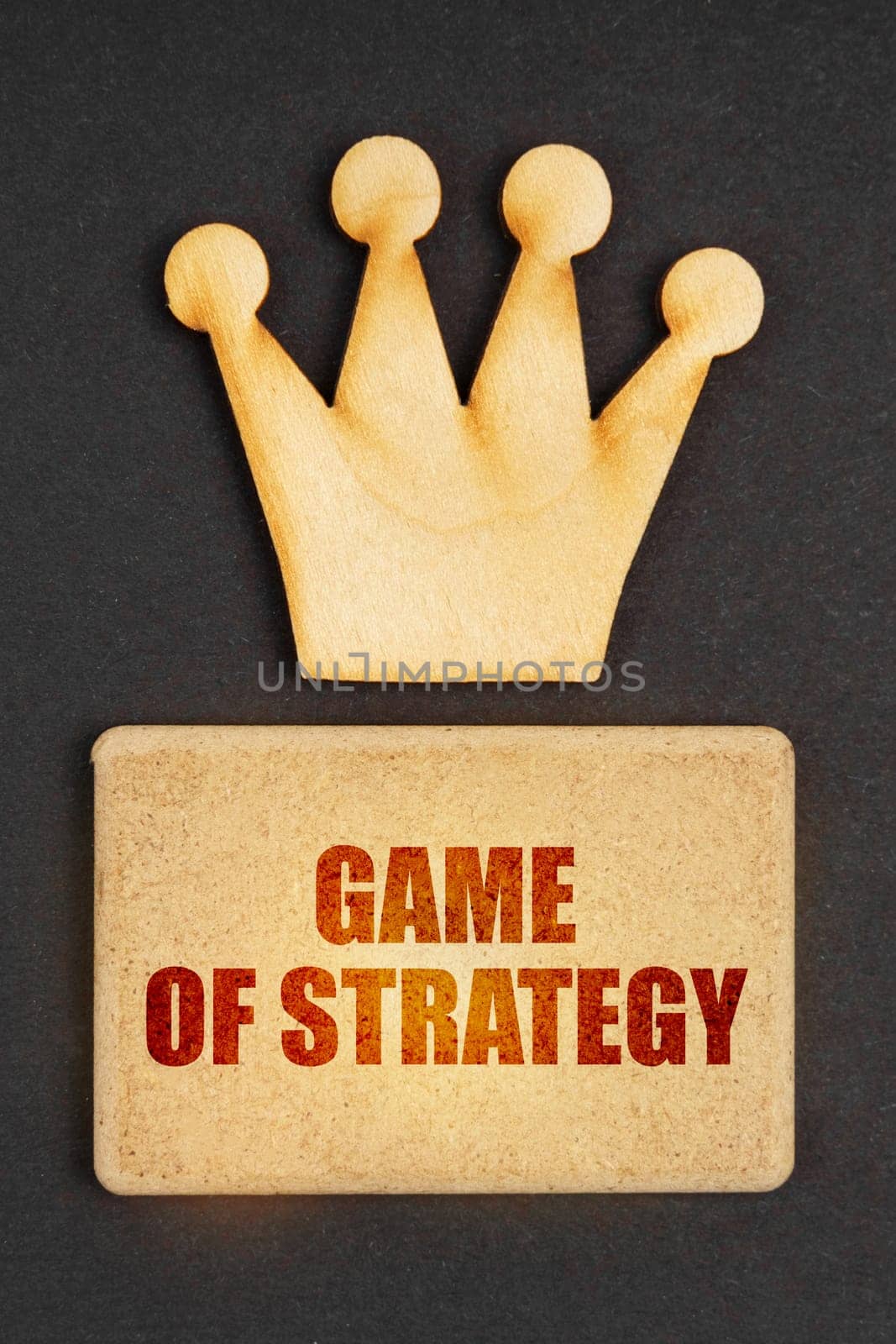 Business concept. On a black background there is a wooden crown of the leader and a sign with the inscription - Game of Strategy