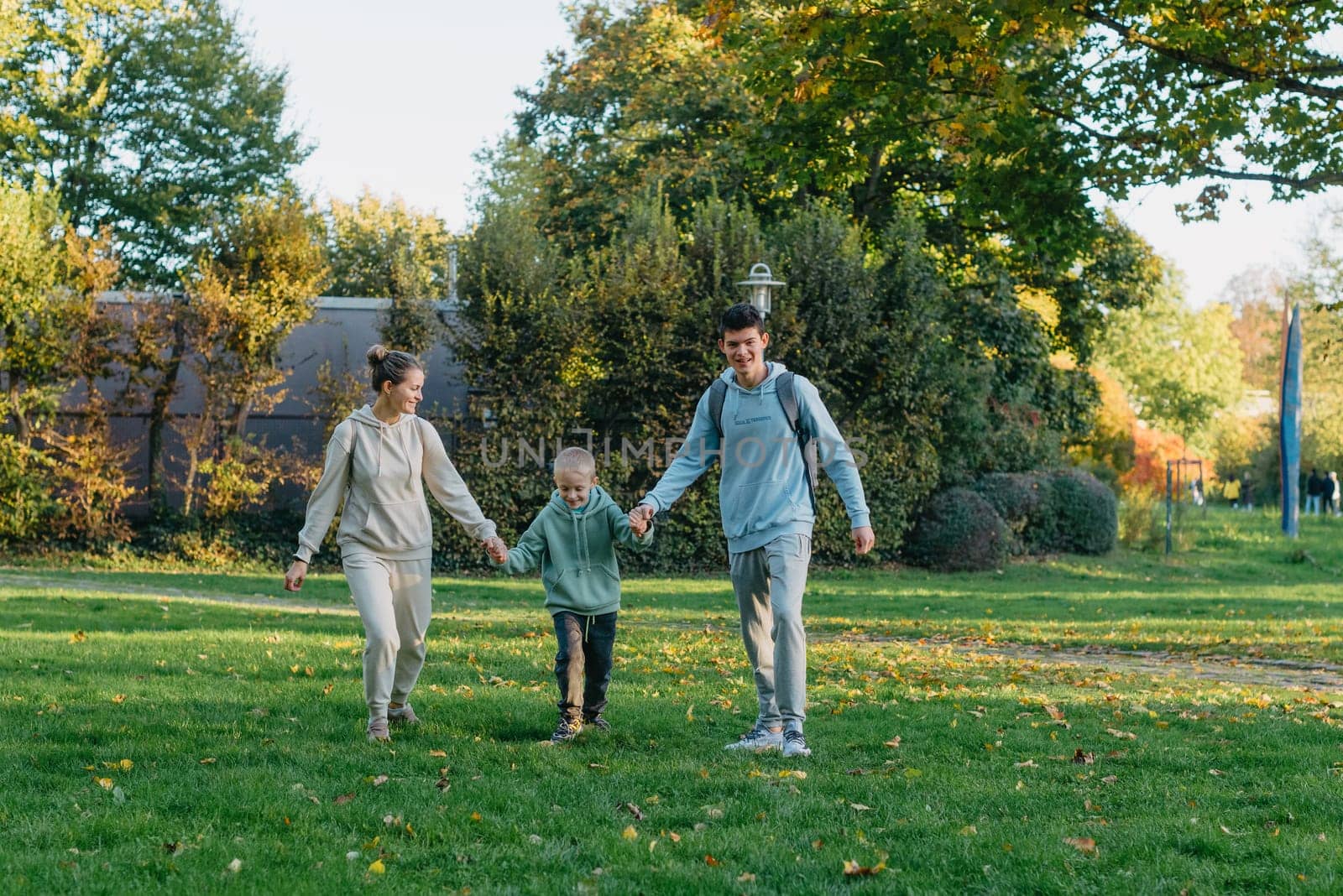 a family mom and 2 sons are having fun, running in the park and jumping. Sons, children, mom, run, play, rejoice, enjoy nature in summer. Family teamwork. Happy family team, running together in field, happily waving their hands. Group of people of different ages. happy family, mom and two sons on an emotional walk. Running and enjoying life in a green field in the park, blue sky, nature.