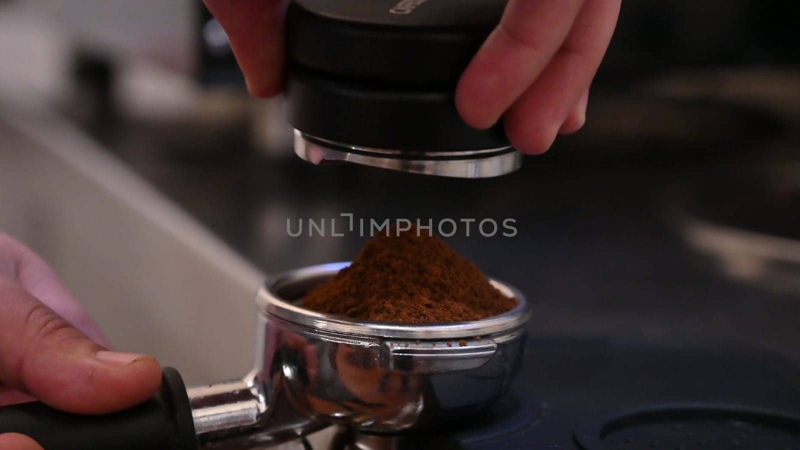 Barista hand holding and pressing tamper on coffee grounds powder in portafilter ready to make cup of coffee. by Peruphotoart